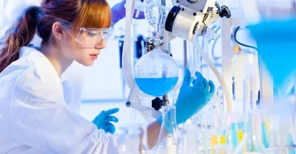 A laboratory technician in safety glasses and gloves running an analysis on a blue process solution