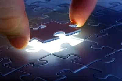 Two hands fitting the final glowing piece into a dark jigsaw puzzle