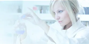 A technician in a white lab coat holding a sample vial up to the light