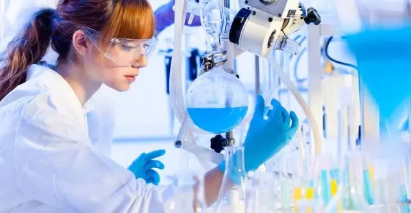 A technician in safety glasses and gloves analysing a blue process solution at the bench