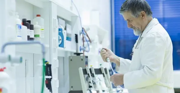 A senior analyst in a white coat working at an instrument bench